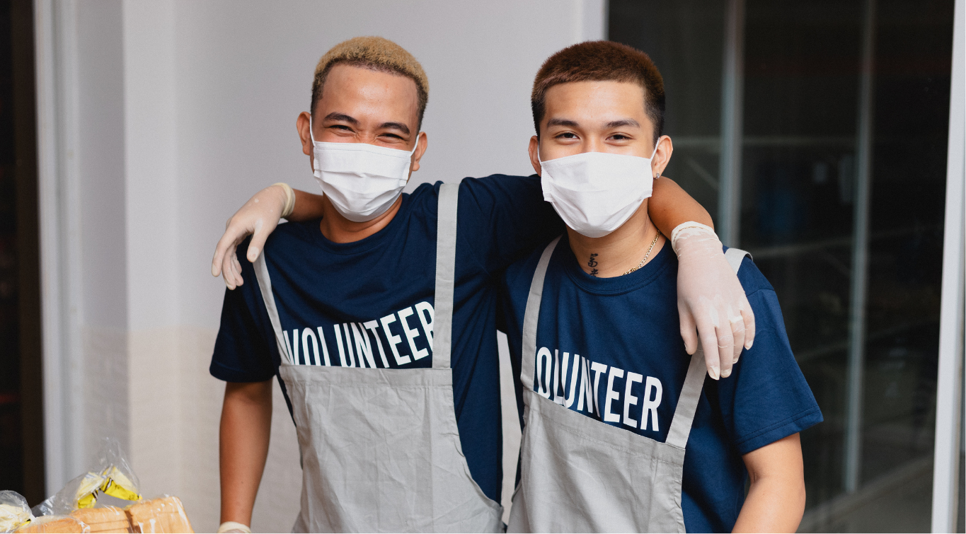 Two volunteers wearing masks and aprons, smiling, symbolizing community support.